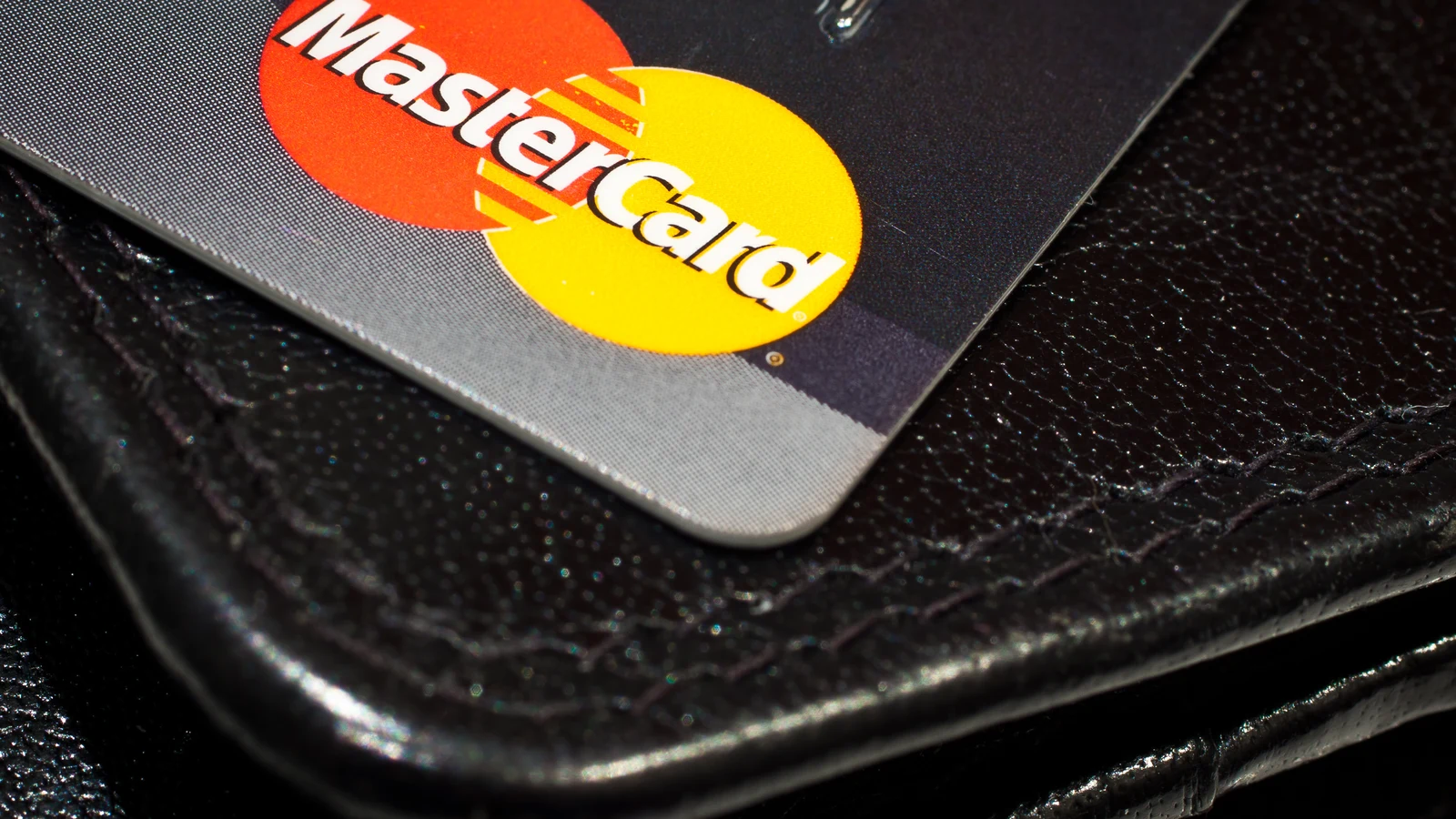 Банковская карта Mastercard лежит на чёрном кожаном кошельке, крупный план