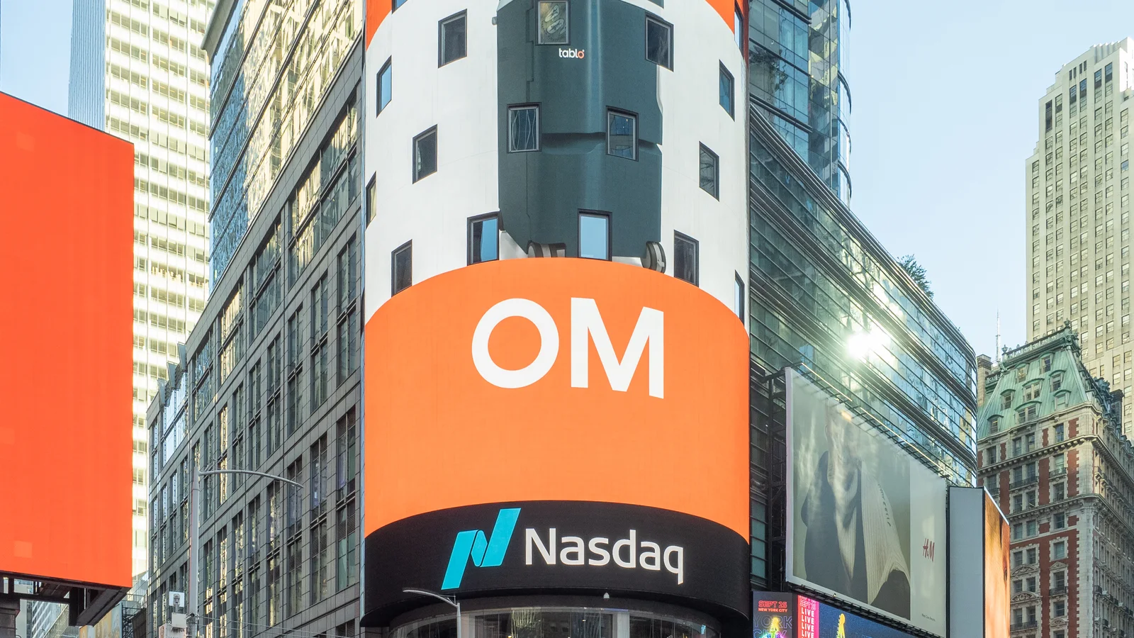 Круглая башня Nasdaq MarketSite на Таймс-сквер с оранжевым экраном и логотипом биржи среди небоскребов