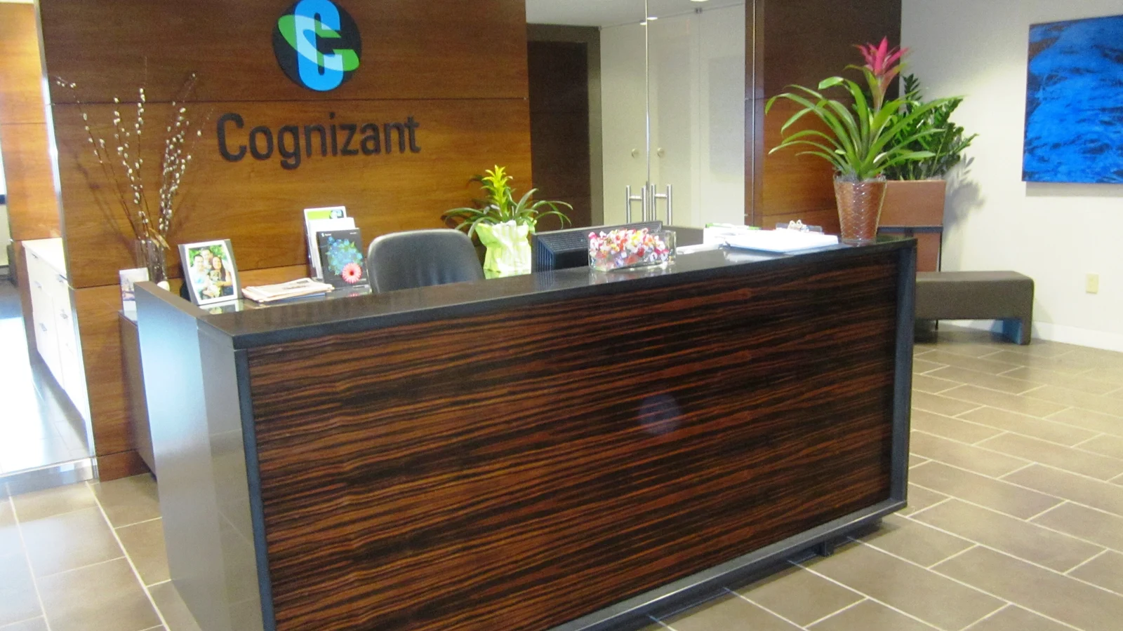 Стойка ресепшен в офисе Cognizant: деревянная стена с логотипом, цветы в горшках и кресло за стойкой